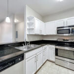 Kitchen with stainless steel appliances, white cabinets and black countertops and a view of the dining room space.