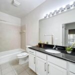 Bathroom with vanity style sink, large mirror with overhead lighting, tiled floors, toilet and standing tub and shower.